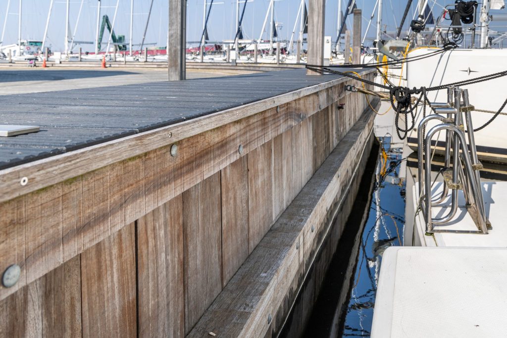Houten damwand constructie langs havenkade met afgemeerde schepen en werkboot