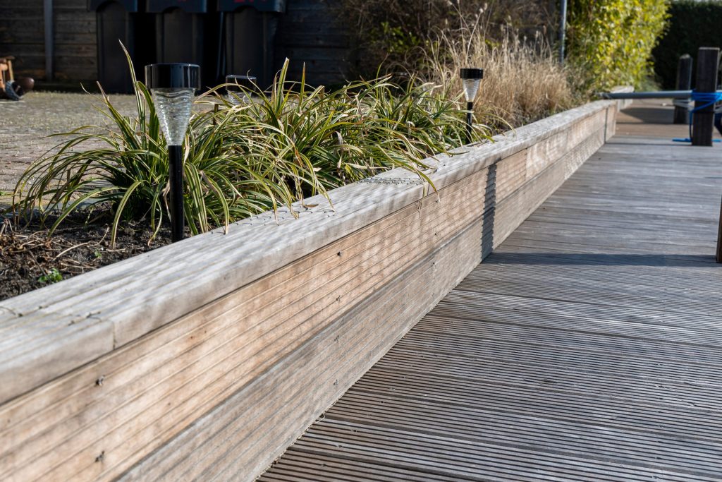Hardhouten vlonderterras met gegroefd terrasplanken langs waterpartij met siergras beplanting en betonnen rand