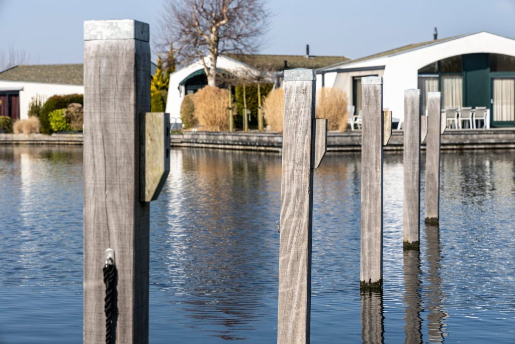 Houten steigerplaatsen met meerpalen aan het water met woningen op de achtergrond