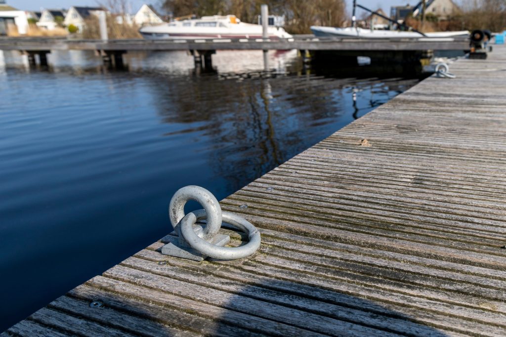 Witte kunststof meerpaal met RVS bevestigingsring op steiger naast jachthaven met boten op achtergrond