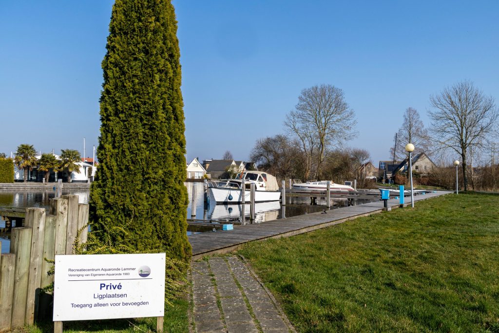 Sluis met sluisdeuren langs waterweg met groenstrook en woonboten op de achtergrond onder blauwe hemel