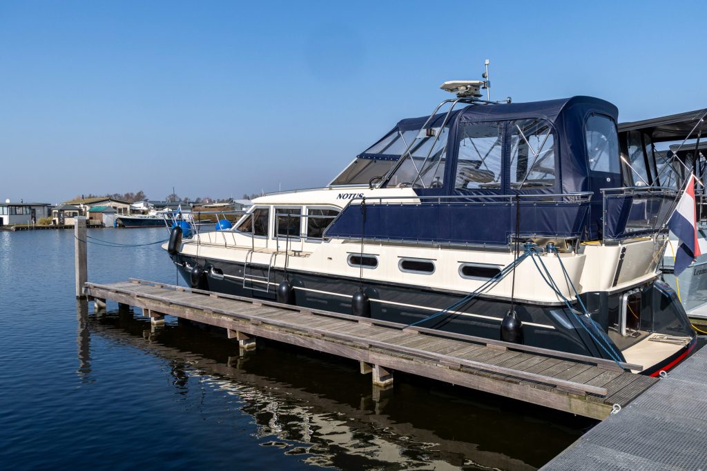Luxe motorjacht afgemeerd aan houten steiger in jachthaven met blauwe lucht