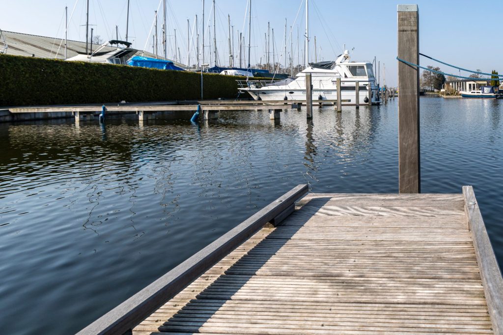 Houten steiger in jachthaven met aangemeerde boten en palen voor waterwerken en aanlegfaciliteiten
