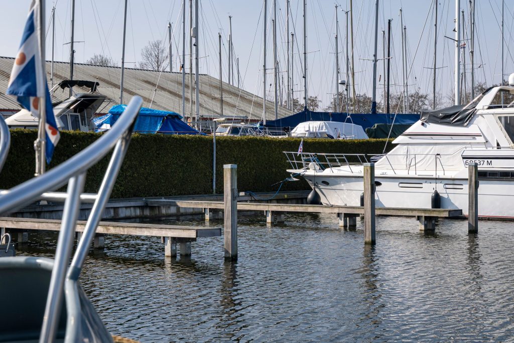 Boot wordt uit het water getakeld met blauwe hijsbanden in jachthaven met steigers en andere boten op achtergrond