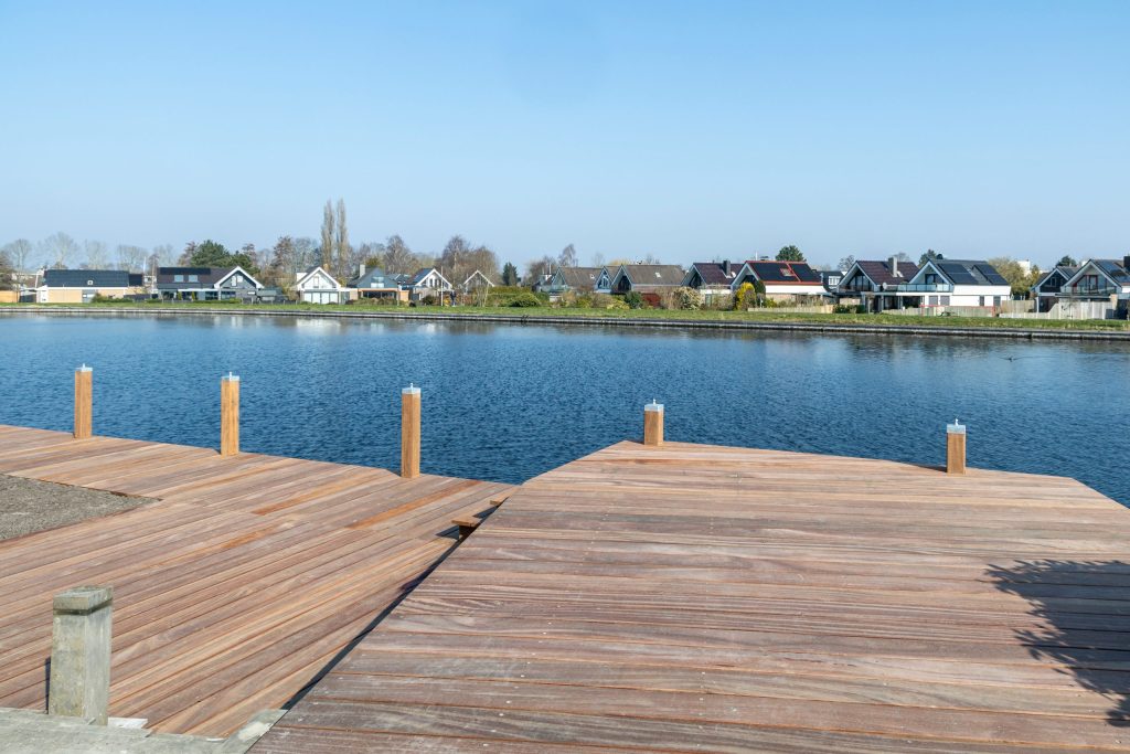 Houten steiger met aanlegpalen aan rustig water met woonwijk op de achtergrond