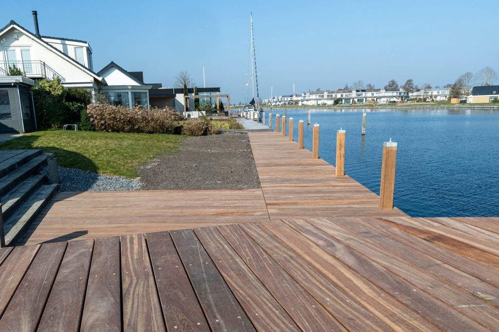 Houten steiger met aanlegpalen langs waterfront met boten op de achtergrond en aangrenzend graspad