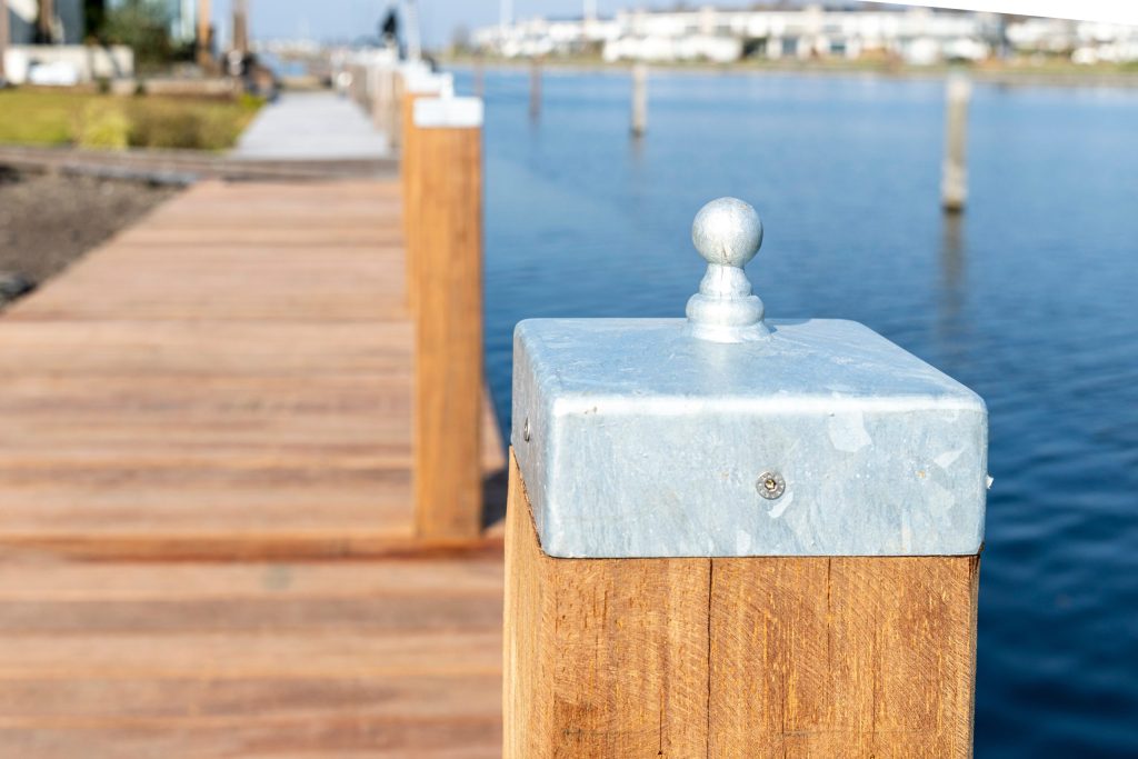 Houten steiger met dukdalven en meerpalen langs waterfront met beschermkappen