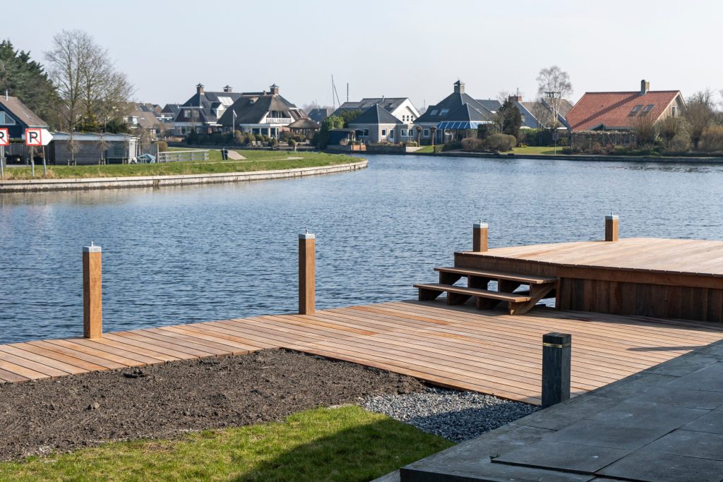 Houten aanlegsteiger met meerpalen aan recreatieplas met uitzicht op woonwijk