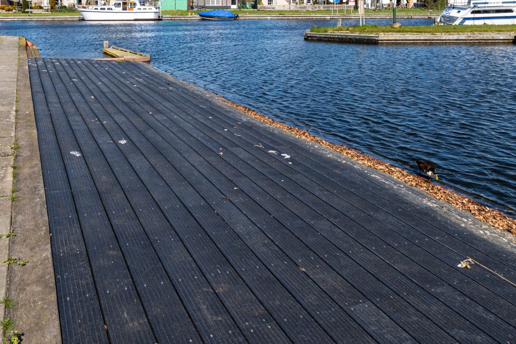 Zwarte houten steiger aangelegd langs waterkant met duurzame vlonderplanken en grindpad