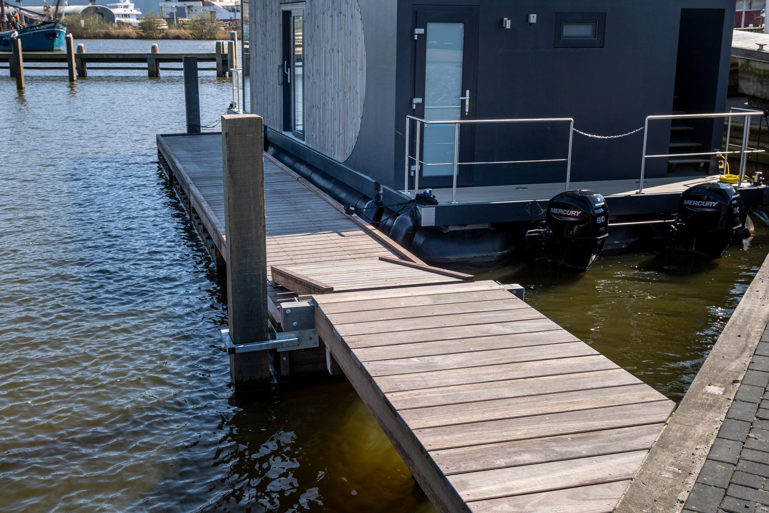 Houten loopsteiger langs woonboot met drijvers en roestvrijstalen hekwerk in de haven