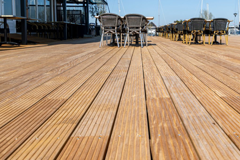 Houten vlonder met hardhouten planken langs het water met steigers en meerpalen op de achtergrond